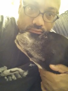 A black and white dog looks up at a man wearing glasses who is leaning on her forehead with his chin while cupping her neck with his hand.